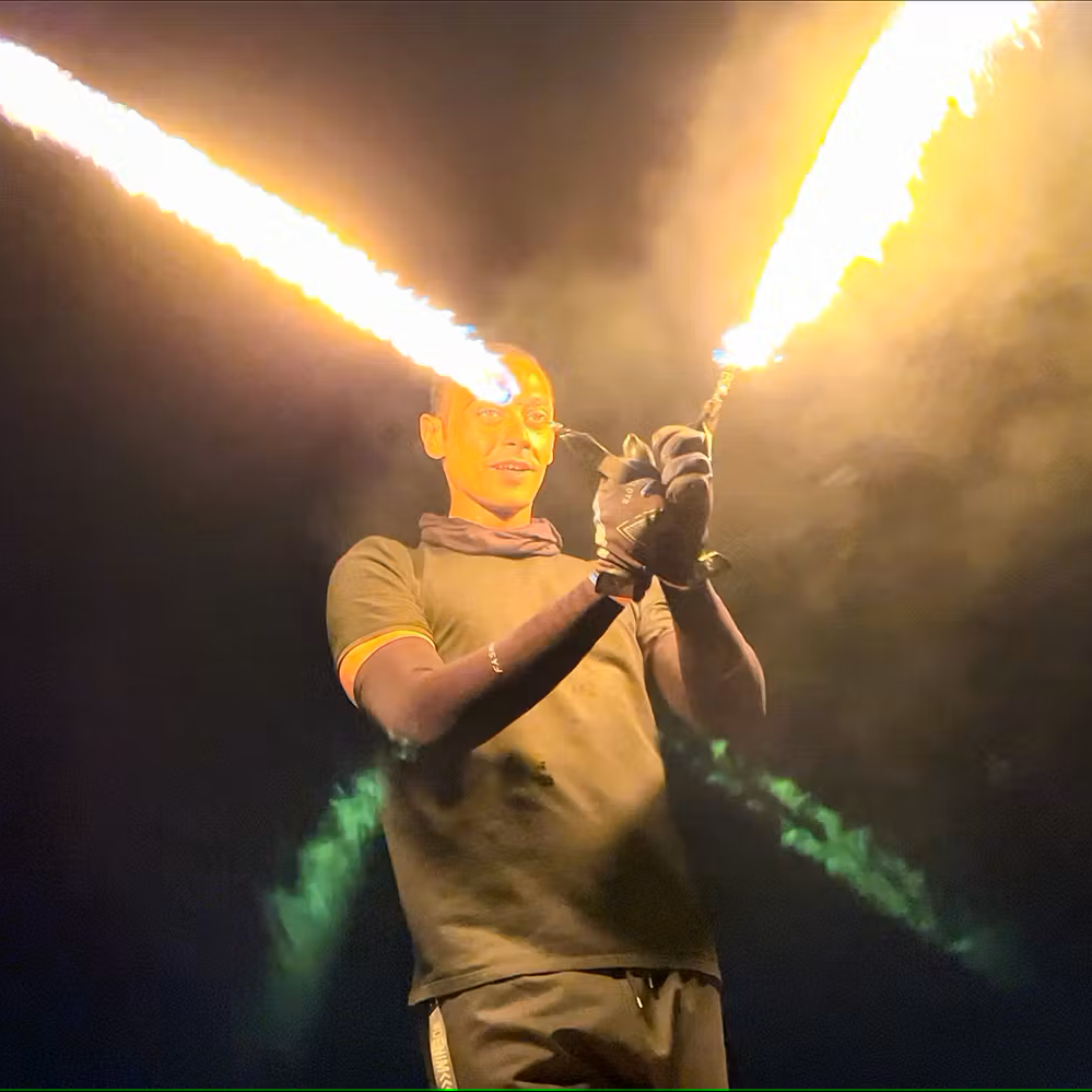 Person holding two flaming torches against a dark background